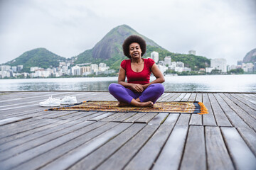 Middle-aged woman meditating sitting on a pier on the edge of the lagoon in Rio de Janeiro.