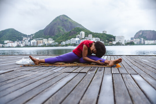 Mulher de meia idade se alongando, praticando ioga, sentada em um pier a beira da lagoa no Rio de Janeiro.