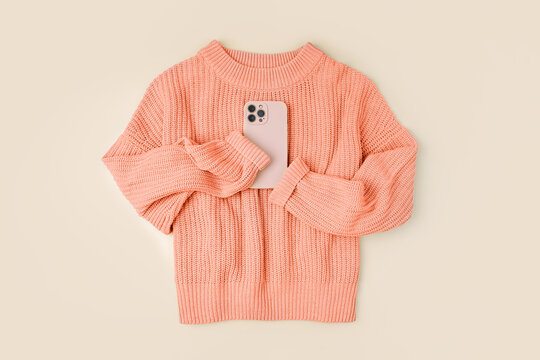 Knitted orange sweater with smartphone. Peach Fuzz - color of the year 2024. Women's warm jumper, stylish autumn or winter clothes. Fashion autumnal outfit. Color trend. 