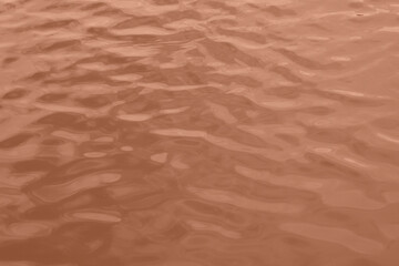 Peach Fuzz toned sea water texture. Pool water with sun reflections. Trendy colour 2024 year.