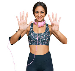 Beautiful brunette woman wearing gym clothes and using headphones showing and pointing up with...