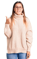 Beautiful caucasian woman wearing wool winter sweater smiling happy and positive, thumb up doing excellent and approval sign