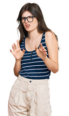 Young beautiful caucasian girl wearing casual clothes and glasses disgusted expression, displeased and fearful doing disgust face because aversion reaction. with hands raised