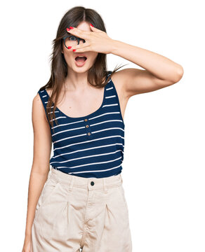 Young beautiful caucasian girl wearing casual clothes and glasses peeking in shock covering face and eyes with hand, looking through fingers with embarrassed expression.