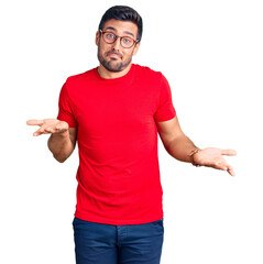 Young hispanic man wearing casual clothes and glasses clueless and confused expression with arms and hands raised. doubt concept.