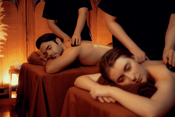 Hot stone massage at spa salon in luxury resort with warm candle light, blissful couple customer...