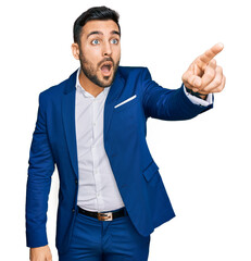 Young hispanic man wearing business jacket pointing with finger surprised ahead, open mouth amazed expression, something on the front