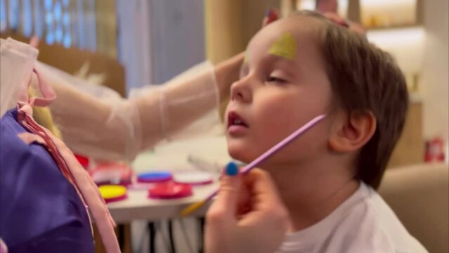 Child animator, woman painting on child's face during holiday. The artist's hand draws on the face of a little boy. Face painting at children holiday, event, birthday party