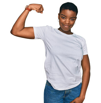 Young african american woman wearing casual white t shirt strong person showing arm muscle, confident and proud of power