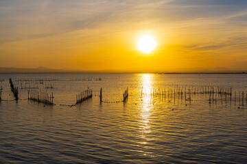 Obraz premium A lake with fish nets and sunny path against the backdrop of an orange sunset