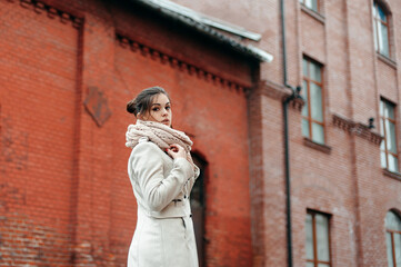 Beautiful girl in a white coat and scarf on the background of a red brick wall