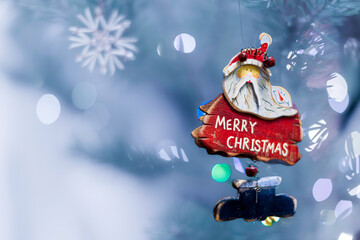 Old handmade wooden toy Santa Claus on the Christmas tree and lights at blurred background.