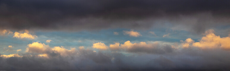 A patch of sky illuminated by the evening sun shines through the dark blue clouds