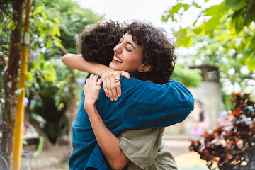 Two women hugging each other on a pleasant date in the park. - obrazy, fototapety, plakaty