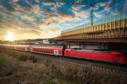 Schneller Zug rast in der Abendd&auml;mmerung unter einem eingeschalten Br&uuml;ckenbauwerk her, Symbolfoto.