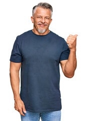 Middle age grey-haired man wearing casual clothes smiling with happy face looking and pointing to the side with thumb up.