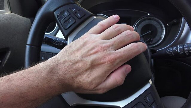 Angry driver honking the car horn in traffic, closeup of hand pushing the steering wheel honk