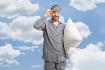 Man in pajamas taking off a sleeping mask and holding a pillow