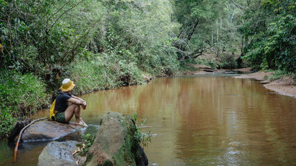 Mujer joven de pelo corto en la orilla de un arroyo descansando en un bosque 