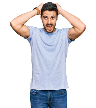 Young hispanic man wearing casual clothes crazy and scared with hands on head, afraid and surprised of shock with open mouth