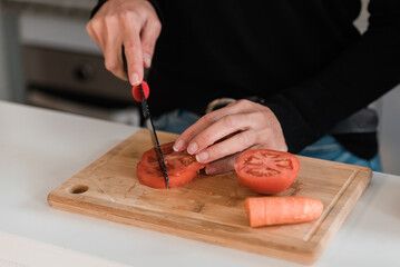 Crop woman cutting tomatoes on board