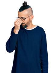 Hispanic man with ponytail wearing casual sweater and glasses tired rubbing nose and eyes feeling fatigue and headache. stress and frustration concept.