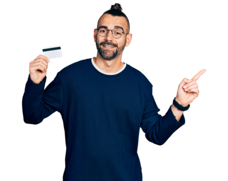 Hispanic man with ponytail holding credit card smiling happy pointing with hand and finger to the side