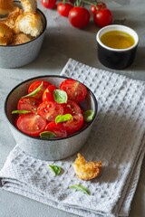 Salad of fresh cherry tomatoes with croutons, basil leaves, spices and aromatic olive oil on a gray background. Panzanella is a Tuscan vegetable salad popular in the summer. Italian Cuisine.