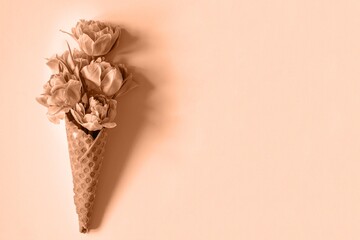 Wafer (waffle) cone with tulips on peach background. Flower ice cream, spring concept with first flowers, mother's day, top view. Color of the Year 2024 Peach Fuzz.