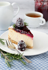 A piece of cheesecake with berry sauce and blackberries on a plate with a cup of tea.