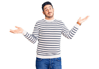 Young hispanic man wearing casual clothes clueless and confused expression with arms and hands...