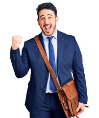Young hispanic man wearing suit and leather bag screaming proud, celebrating victory and success...