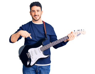 Young hispanic man playing electric guitar smiling happy pointing with hand and finger