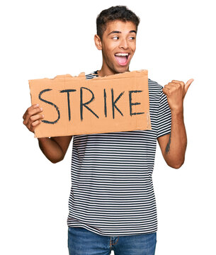 Young handsome african american man holding strike banner cardboard pointing thumb up to the side smiling happy with open mouth