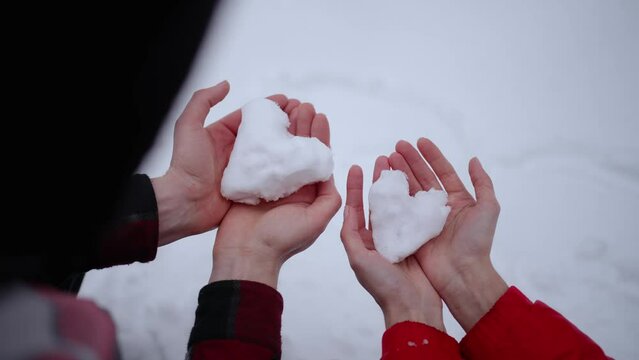 A man and a woman hold snow in the shape of a heart
