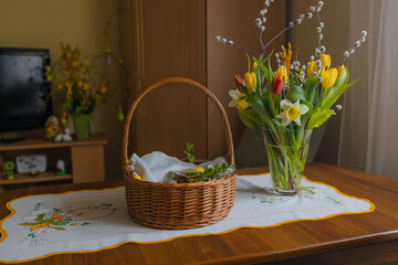 Traditional Easter basket on family table in Poland. Easter modern eggs, easter bread, ham, beets, butter, in wicker basket decorated with green boxwood branches and flowers on rustic wooden table