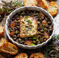 Baked Feta cheese with olives, olive oil and aromatic herbs served in a baking dish, close up view