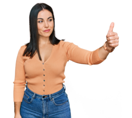 Young hispanic woman wearing casual clothes looking proud, smiling doing thumbs up gesture to the side