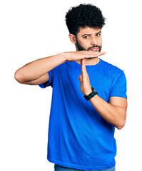 Young arab man with beard wearing casual blue t shirt doing time out gesture with hands, frustrated...