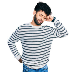 Obraz premium Young arab man with beard wearing casual striped sweater stretching back, tired and relaxed, sleepy and yawning for early morning