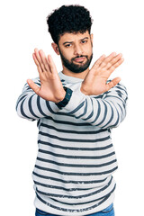 Naklejka premium Young arab man with beard wearing casual striped sweater rejection expression crossing arms doing negative sign, angry face