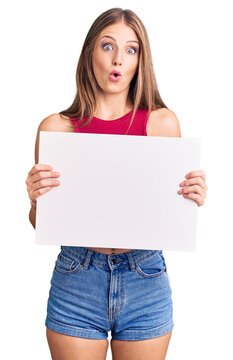 Young beautiful blonde woman holding blank empty banner scared and amazed with open mouth for surprise, disbelief face