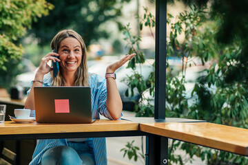 Seated in the café's garden, a businesswoman efficiently coordinates her call and online work,...