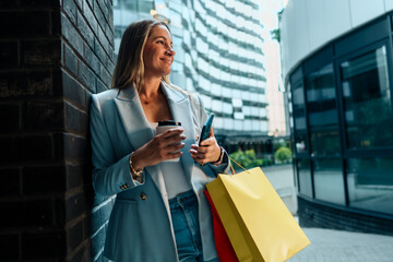 In the cityscape, a businesswoman carrying shopping bags effortlessly juggles her phone, coffee, and the journey back home.