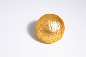 Praline chocolate ball wrapped in gold foil, golden wrapper candy on white background - obrazy, fototapety, plakaty