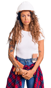 Young hispanic woman with tattoo wearing hardhat and builder clothes depressed and worry for distress, crying angry and afraid. sad expression.