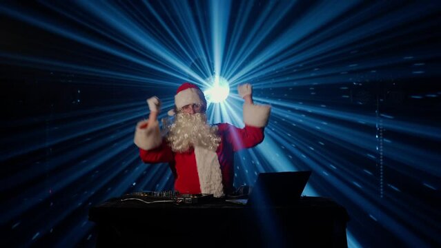 DJ Santa Claus mixing tracks in a nightclub at a Christmas and New Year party or Corporate events. Senior disc jockey as Santa listening music, headphones, laptop, mixer controller player, turntable.