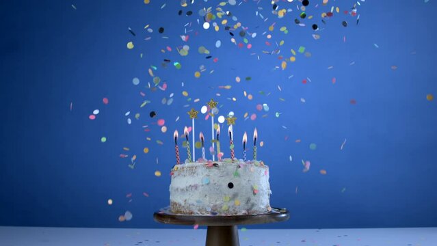 Anniversary celebration of cake with candles on blue background with confetti falling in slow-motion, party celebration marking important event