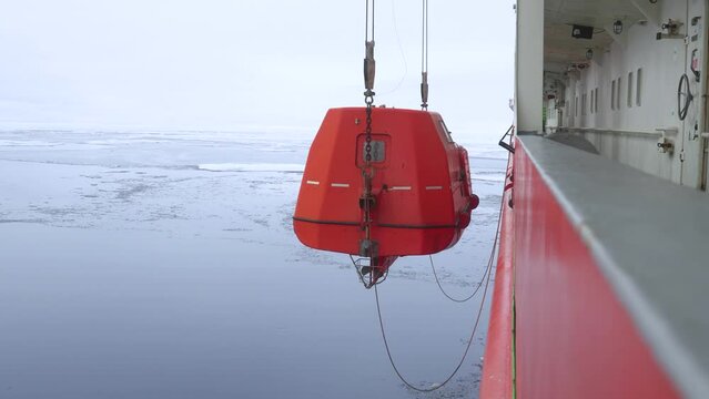 Lifeboat is lowered down. rescue boat. Orange rescue boat is hanging on ropes at side of vessel