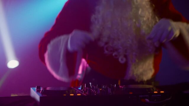 DJ Santa Claus mixing tracks in a nightclub at a Christmas and New Year party or Corporate events. Senior disc jockey as Santa listening music, headphones, laptop, mixer controller player, turntable.